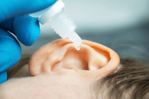 a person laying horizontally with focus on their ear with a tube of Hydrogen Peroxide going into the ear